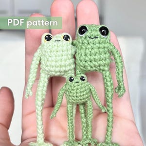 May include: Three small crocheted frogs in varying shades of light and medium green yarn. Each frog features large black plastic eyes and long, thin limbs. The text "PDF pattern" is visible in the upper left corner of the image.