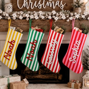 Könnte beinhalten: Vier gestreifte Weihnachtsstrümpfe hängen in einer Reihe in den Farben Gelb, Grün, Rot und Pink. Jeder Strumpf trägt einen Namen in weißer oder roter Schreibschrift: Noah, Noah, Cassidy und Sophia. Sie hängen an einem Kaminsims.