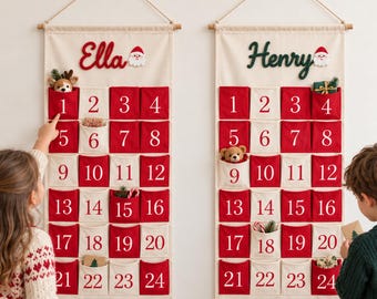 May include: Two vertical fabric advent calendars hanging on a wall. Each features a cream-colored background with red and cream pockets numbered 1 through 24. The names Ella and Henry are embroidered at the top, accompanied by a small Santa icon.