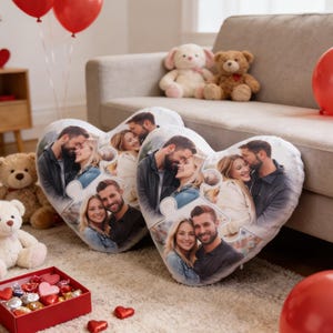 May include: Two heart-shaped cushions featuring a couple's photo, designed as a jigsaw puzzle. Red balloons, teddy bears, and a box of chocolates are arranged nearby. The setting suggests a romantic celebration on a cream-colored rug.