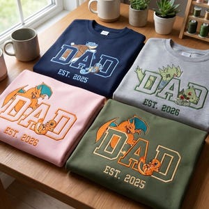 May include: Four crewneck sweatshirts in navy, light grey, light pink, and olive green. Each features embroidered text DAD with a year and a cartoon character. The navy shirt says DAD EST. 2025, grey says DAD EST. 2026, pink says DAD EST. 2026, and olive says DAD EST. 2025.
