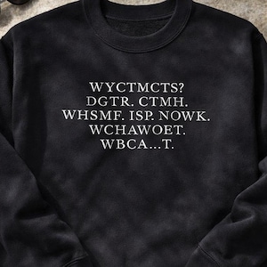 Könnte beinhalten: Schwarzes Sweatshirt mit weißem Text: WYCTMCTS? DGTR. CTMH. WHSMF. ISP. NOWK. WCHAWOET. WBCA...T. Eine Sonnenbrille liegt oben links. Das Sweatshirt liegt auf einer neutralen Oberfläche.