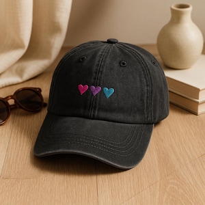 Può includere: Un cappellino da baseball nero con tre cuori ricamati in rosa, viola e blu. Il cappellino ha una visiera curva e un classico design a sei pannelli. Realizzato in tessuto morbido e resistente.