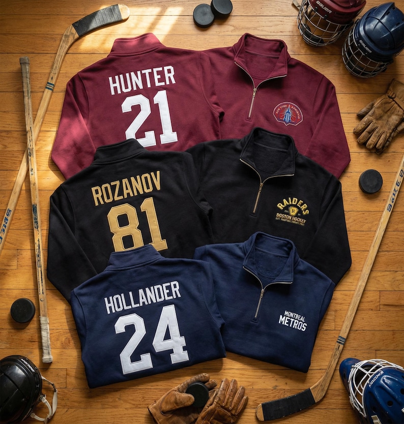 May include: A collection of hockey-themed quarter-zip pullovers in burgundy, black, and navy blue. Each pullover features a player's name and number on the back, with team logos on the front. Hockey sticks, pucks, helmets, and gloves are arranged around the pullovers.