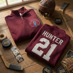 May include: A burgundy zip-up sweatshirt with a "New York Admirals" logo and a burgundy jersey with "Hunter 21" in white. Hockey equipment, including a helmet, pucks, and a stick, are arranged on a wooden surface.