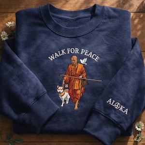 May include: Navy blue sweatshirt with embroidered design. Features the text "WALK FOR PEACE" above an image of a monk with a dog and a dove. The sleeve has the word "ALOKA" with a peace symbol.