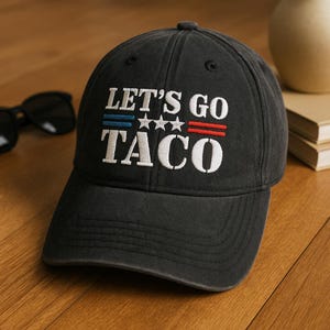 Könnte beinhalten: Eine schwarze Baseballkappe mit dem gestickten Text "LET'S GO TACO" in Weiß. Der Text ist mit blauen und roten Streifen und drei weißen Sternen verziert. Die Kappe ist aus weichem, abgenutztem Material.