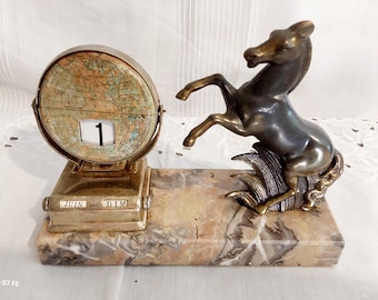 May include: An antique desk calendar with a globe-shaped dial displaying the date as "1". The calendar is made of brass and sits on a marble base, with a bronze horse sculpture on the right side.