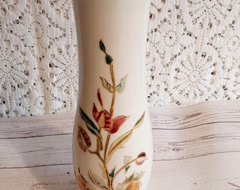 Peut inclure: Un vase en céramique crème de forme élancée et allongée. Le vase est orné d'un motif floral avec des accents rouges, verts et dorés. Le bord du vase est orné d'une bordure dorée. Le vase mesure environ 25 cm de haut.