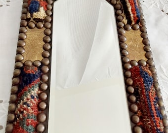 Op de afbeelding: Een rechthoekige spiegel met een decoratief frame. Het frame is gemaakt van hout en bedekt met een kleurrijke stof met een geometrisch patroon. Het frame is ook versierd met metalen studs.