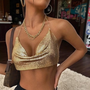 May include: A gold metallic halter top with a draped neckline. The top is paired with a layered gold chain necklace. The image shows a close-up of the top and necklace.