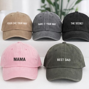 Puede incluir: Cinco gorras de béisbol en varios colores: beige, gris, negro, rosa y verde oliva. Cada gorra tiene texto blanco. Los textos en las gorras dicen: "YOUR CAP, YOUR WAY", "HAVE IT YOUR WAY", "THE SECRET", "MAMA" y "BEST DAD".