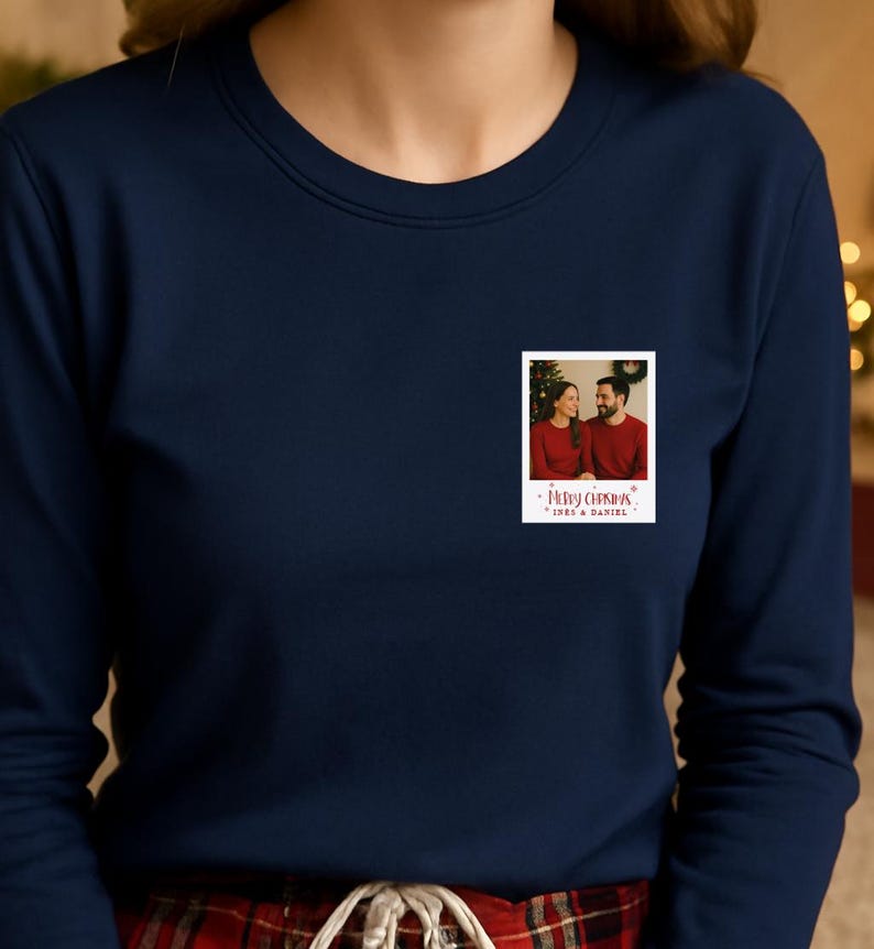 May include: Navy blue sweatshirt with a small, rectangular photo print. The photo shows a couple in red shirts with a Christmas tree in the background. The text "Merry Christmas" and names are below the photo.