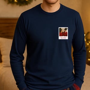 May include: Navy blue long-sleeve shirt with a small, rectangular photo print on the chest. The photo shows a couple in red sweaters. The text "Merry Christmas" and "Love & Family" is printed below the photo.