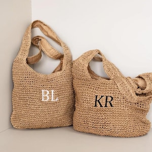 May include: Two woven straw tote bags. One bag has the white embroidered letters "BL", and the other has the black embroidered letters "KR". The bags have a shoulder strap and are made of a light brown material.