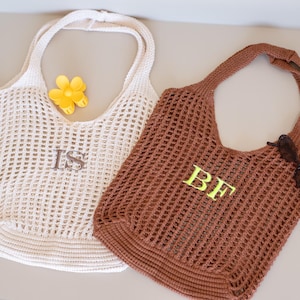 May include: Two open-weave tote bags. One is off-white with the initials "IS" and a yellow flower. The other is brown with the initials "BF" and sunglasses. Both bags have long handles.
