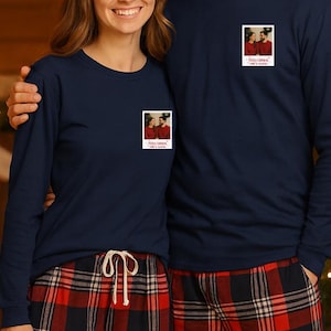 May include: Matching navy blue long-sleeve shirts and red plaid pajama pants. Each shirt has a small photo print on the chest. The background includes a Christmas tree and fireplace, suggesting a holiday theme.