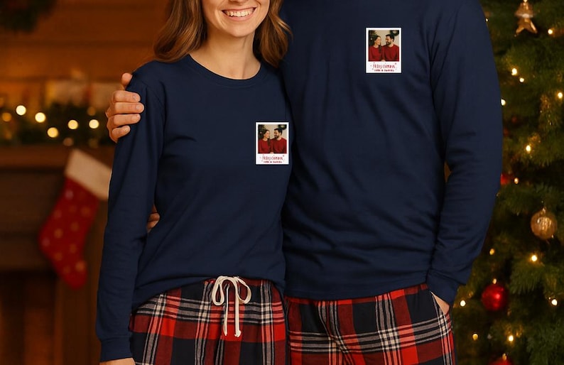 May include: Matching navy blue long-sleeve shirts and red plaid pajama pants. Each shirt has a small photo print on the chest. The background includes a Christmas tree and fireplace, suggesting a holiday theme.