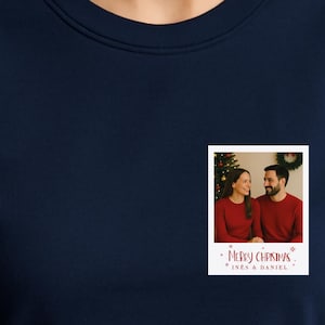 May include: Navy blue sweatshirt with a small, rectangular photo print. The photo shows a couple in red sweaters in front of a Christmas tree. The print includes the text "Merry Christmas" and the names "Ines & Daniel".
