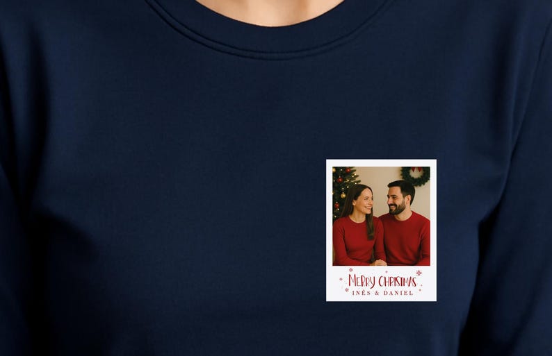 May include: Navy blue sweatshirt with a small, rectangular photo print. The photo shows a couple in red sweaters in front of a Christmas tree. The print includes the text "Merry Christmas" and the names "Ines & Daniel".