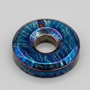 May include: A circular, iridescent blue object with a central hole. The surface has a marbled pattern with streaks of lighter blue and hints of purple and orange. The object appears to be made of metal.