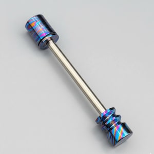 May include: A metal dab tool with a silver shaft and two ends with a colorful, swirling pattern of blues, purples, and yellows. The ends are cylindrical and textured, with a polished finish.