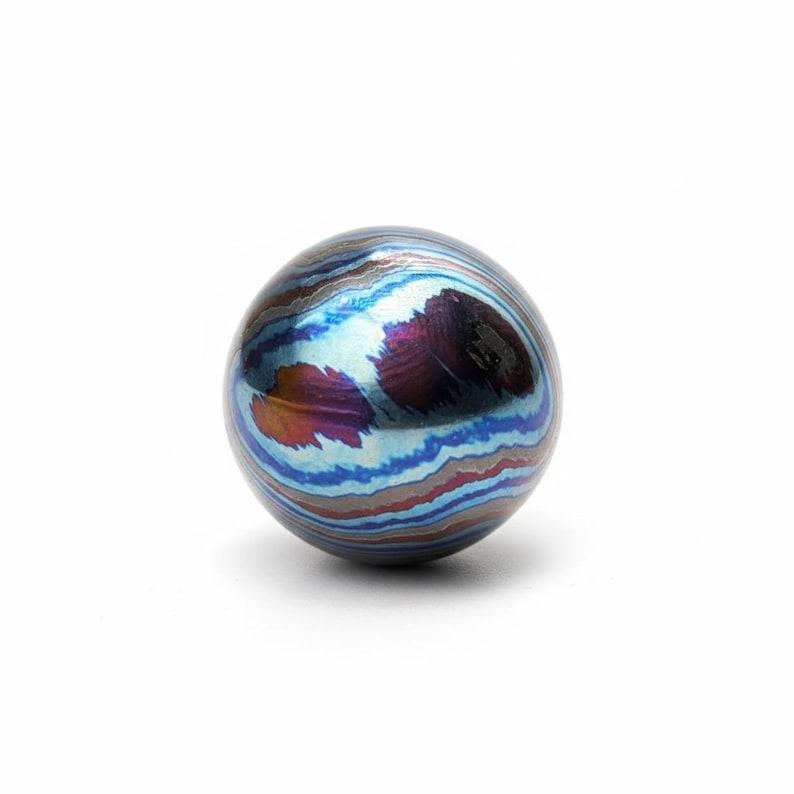 Pu&ograve; includere: Un oggetto sferico con un sorprendente motivo a spirale di blu, viola e arancione. L'orbita sembra metallica e ha una superficie lucida. Il design ricorda una galassia in miniatura o una gemma. La sfera misura circa 3 cm di diametro.