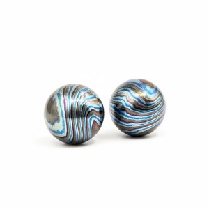 Pu&ograve; includere: Due oggetti sferici con un motivo a vortice di tonalit&agrave; blu, argento e marrone. Le sfere hanno una lucentezza metallica e sono poste su uno sfondo bianco. Il design ricorda un effetto marmorizzato.