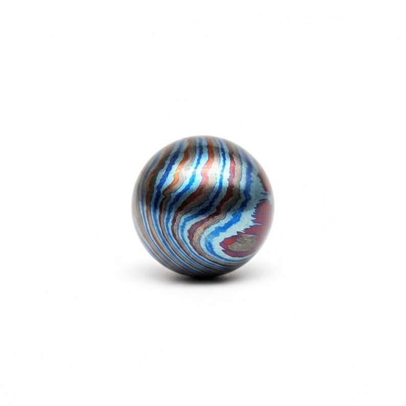 Pu&ograve; includere: Oggetto sferico con un motivo a vortice di blu, rosso e grigio argento. La palla ha un aspetto metallico lucido e una superficie liscia. Il design ricorda le venature del legno o l'acqua che scorre.
