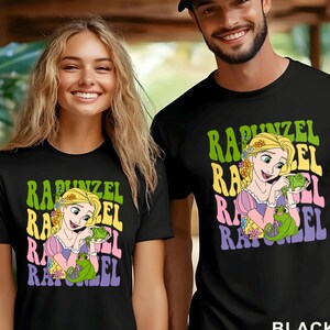 May include: Black t-shirts featuring a colorful graphic of Rapunzel holding a green chameleon, with the name "Rapunzel" in a retro font. The shirts are worn by a man and a woman.