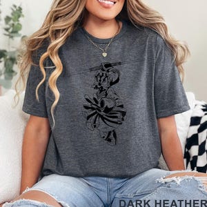 Op de afbeelding: Donkergrijs t-shirt met een zwart grafisch ontwerp. De afbeelding is een gestileerde illustratie van een personage. De tekst "DARK HEATHER" staat onderaan de afbeelding.