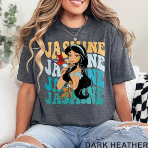 May include: Dark heather gray t-shirt featuring a graphic of Princess Jasmine with the text "Jasmine" in a retro font. The design includes a parrot and a monkey. The words "Dark Heather" are printed at the bottom.