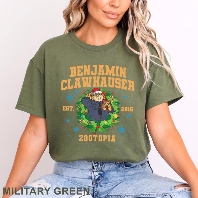 以下が含まれることがあります： 「BENJAMIN CLAWHAUSER」の文字と、サンタ帽をかぶったキャラクターの漫画の画像が描かれた、ミリタリーグリーンのTシャツ。Tシャツには「EST. 2016」と「ZOOTOPIA」の文字も含まれています。