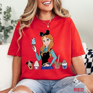 May include: Red t-shirt featuring a cartoon illustration of a character holding an ice cream cone. The character has red hair and is wearing a black and blue outfit. Several ice cream treats are also depicted on the shirt.