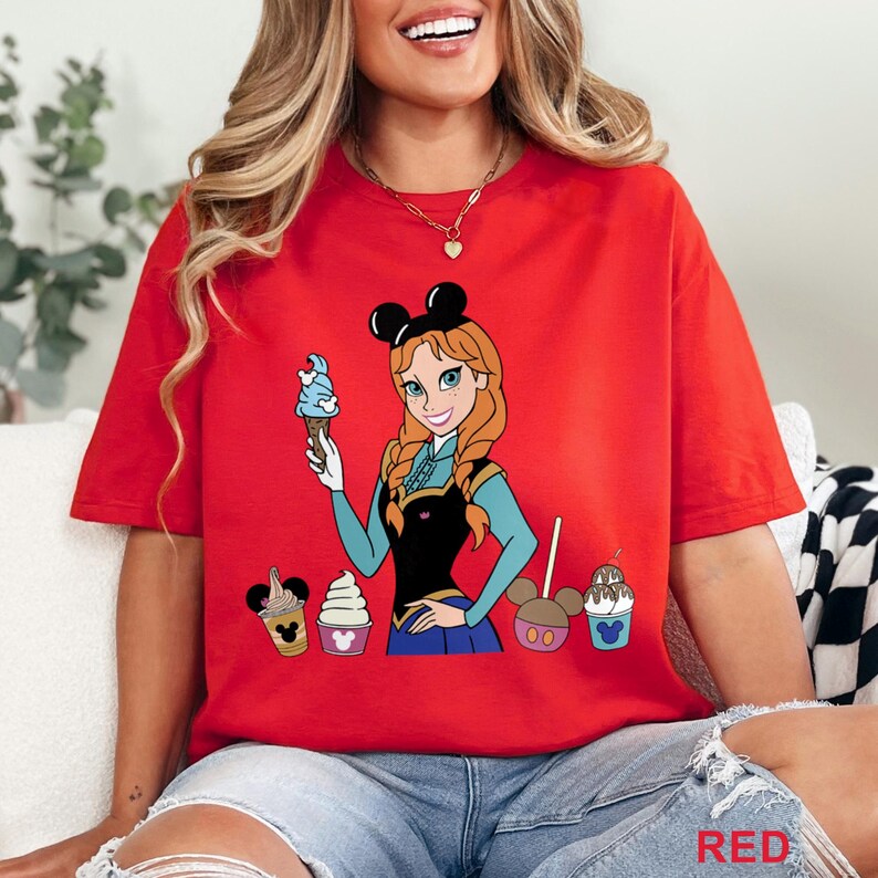 May include: Red t-shirt featuring a cartoon illustration of a character holding an ice cream cone. The character has red hair and is wearing a black and blue outfit. Several ice cream treats are also depicted on the shirt.