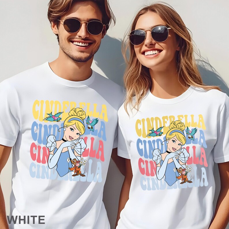 May include: White t-shirts featuring a colorful Cinderella graphic. The design includes the word "Cinderella" in stacked, retro-style lettering, along with an illustration of Cinderella and birds. The word "WHITE" is at the bottom.