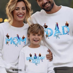 Op de afbeelding: Witte sweatshirts met de woorden "MOM", "DAD" en "BIRTHDAY BOY" in blauw, met personages uit een populaire animatiefilm. De sweatshirts worden gedragen door een gezin van drie, lachend in de camera.