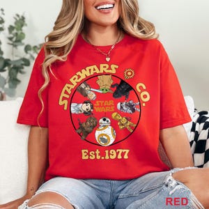 Peut inclure: T-shirt rouge avec un motif circulaire repr&eacute;sentant des personnages de Star Wars, le texte "STARWARS CO." et "Est. 1977". Le motif comprend des personnages comme BB-8, Chewbacca, et d'autres. Le mot "RED" est en bas.