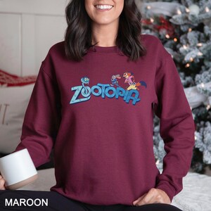 May include: Maroon sweatshirt featuring the word "Zootopia" in blue, with cartoon characters. The sweatshirt is a solid maroon color. The word "MAROON" is printed at the bottom of the image.
