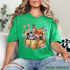 Puede incluir: Camiseta verde irland&eacute;s con un dise&ntilde;o de Judy Hopps y Nick Wilde de Zootopia, enmarcado por flores y placas de polic&iacute;a. La camiseta tiene mangas cortas y cuello redondo. El texto "IRISH GREEN" est&aacute; en la parte inferior.