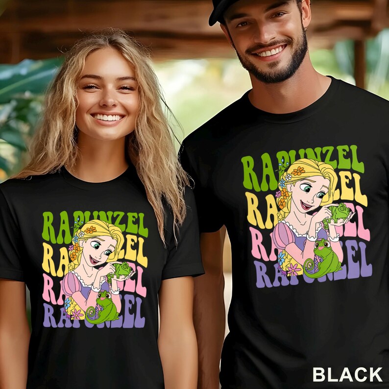 May include: Black t-shirts featuring a colorful graphic of Rapunzel holding a green chameleon, with the name "Rapunzel" in a retro font. The shirts are worn by a man and a woman.