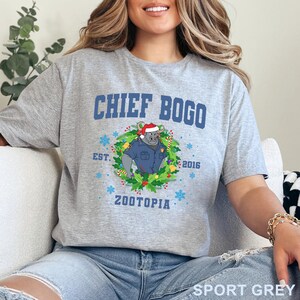 以下が含まれることがあります： 「CHIEF BOGO」の文字と、サンタ帽とリースをつけたズートピアのキャラクターの漫画の画像がプリントされたスポーツグレーのTシャツ。「EST. 2016」と「ZOOTOPIA」の文字も含まれています。