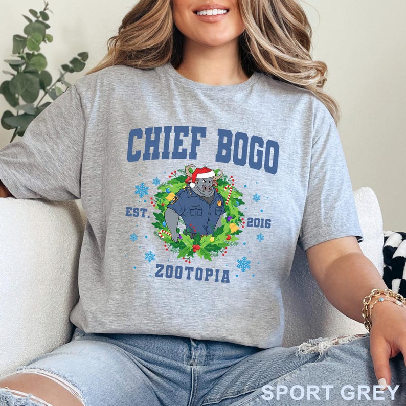 以下が含まれることがあります： 「CHIEF BOGO」の文字と、サンタ帽とリースをつけたズートピアのキャラクターの漫画の画像がプリントされたスポーツグレーのTシャツ。「EST. 2016」と「ZOOTOPIA」の文字も含まれています。