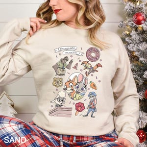 Pu&ograve; includere: Felpa color sabbia con personaggi dei cartoni animati e la scritta "You can be whatever you wish to be". Il design include una ciambella, un distintivo della polizia e vari personaggi animali di un popolare film d'animazione.