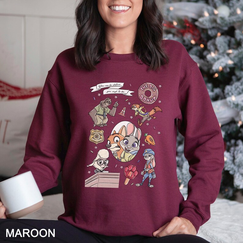 Pu&ograve; includere: Felpa bordeaux con personaggi dei cartoni animati e la scritta "You can be whatever you wish to be!" e "The Big Donut". Il design include un distintivo della polizia, una carota e altre illustrazioni di personaggi.