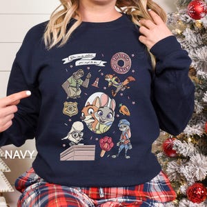 Pu&ograve; includere: Felpa blu navy con personaggi dei cartoni animati e la scritta "THE BIG DONUT". Il design include un distintivo della polizia, un bradipo, una volpe, un coniglio e altri personaggi. &Egrave; presente anche il testo "You can be whatever you wish to be".