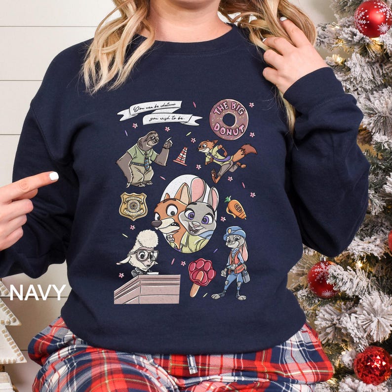 Pu&ograve; includere: Felpa blu navy con personaggi dei cartoni animati e la scritta "THE BIG DONUT". Il design include un distintivo della polizia, un bradipo, una volpe, un coniglio e altri personaggi. &Egrave; presente anche il testo "You can be whatever you wish to be".