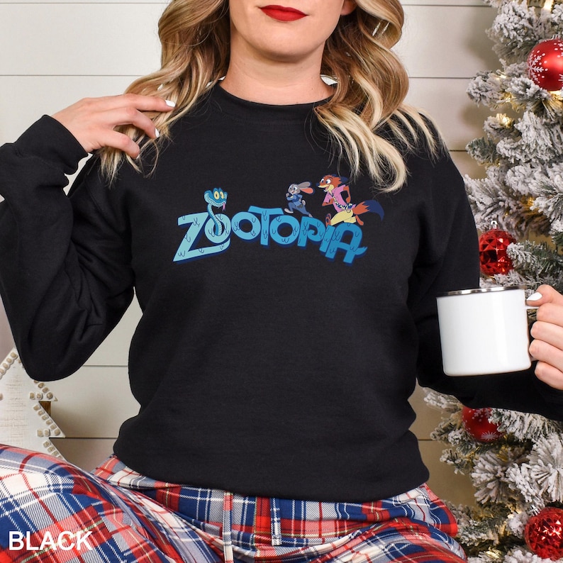 May include: Black crewneck sweatshirt featuring the word "Zootopia" in blue, with cartoon characters. The sweatshirt is a long-sleeved top. The word "BLACK" is printed at the bottom of the image.
