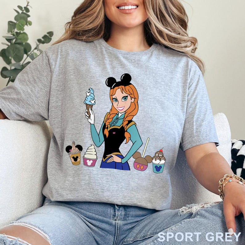 May include: Sport grey t-shirt featuring a cartoon illustration of a character holding an ice cream cone, with several themed desserts. The character has red hair and is wearing a black and blue outfit. The shirt has the words "SPORT GREY" printed at the bottom.