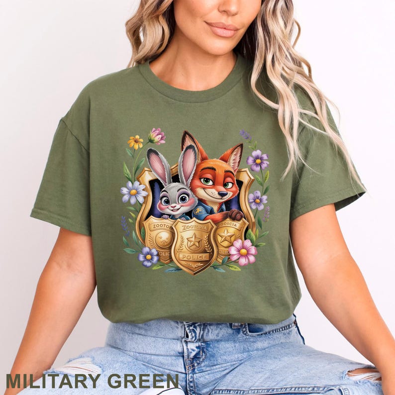 Puede incluir: Camiseta verde militar con un gr&aacute;fico colorido de un zorro y un conejo de Zootopia, enmarcado por flores y escudos de polic&iacute;a. Un estilo casual y c&oacute;modo.